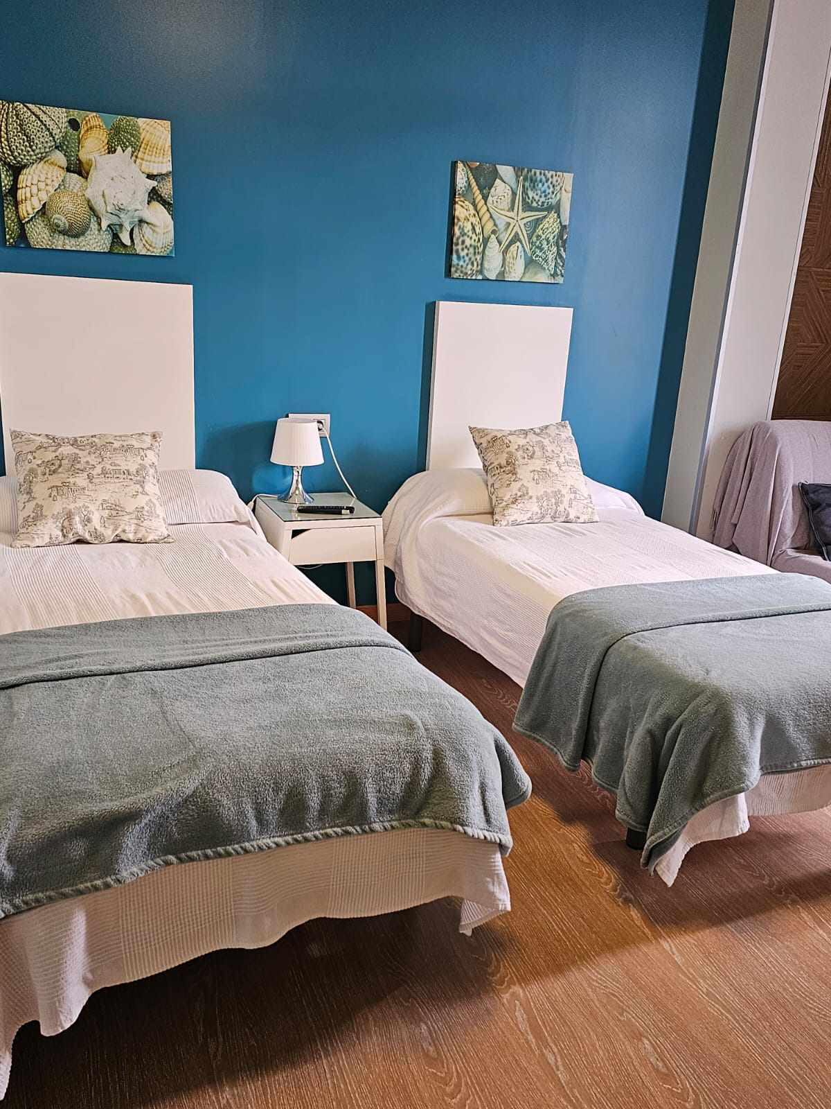 habitación doble con dos camas con mantas de color azul y blanco, y la pared en color azul. Hay dos camas hechas cada cama tiene un cuadro de decoración encima de la misma