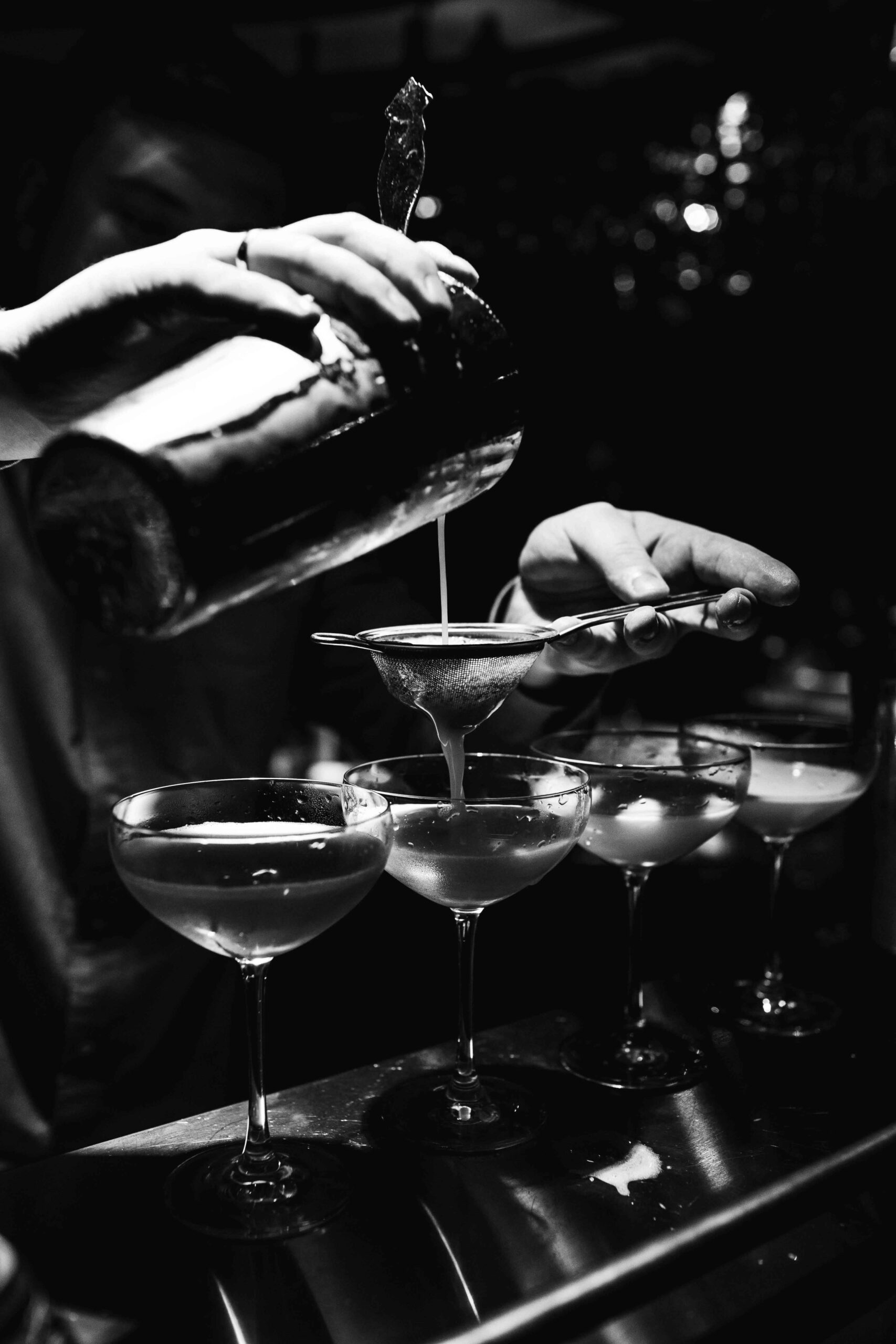 foto en blanco y negro de un primer planop de unas manos sirviendo cocteles en vasos de champagne